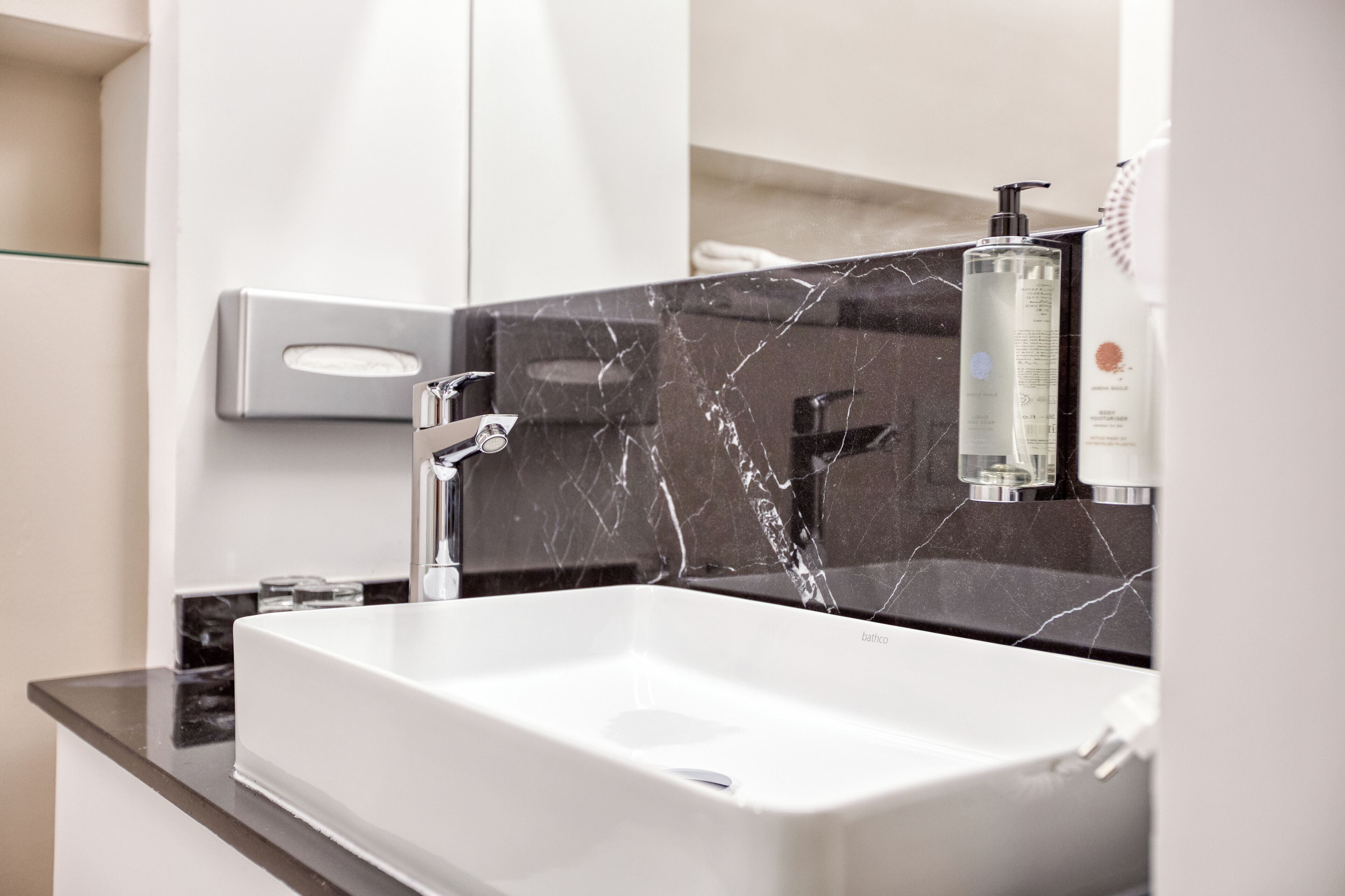 A modern bathroom with a white sink, black marble backsplash, and a mirror.