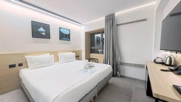 A hotel room with a bed, a desk, a chair, a window with curtains, and a flat-screen TV.