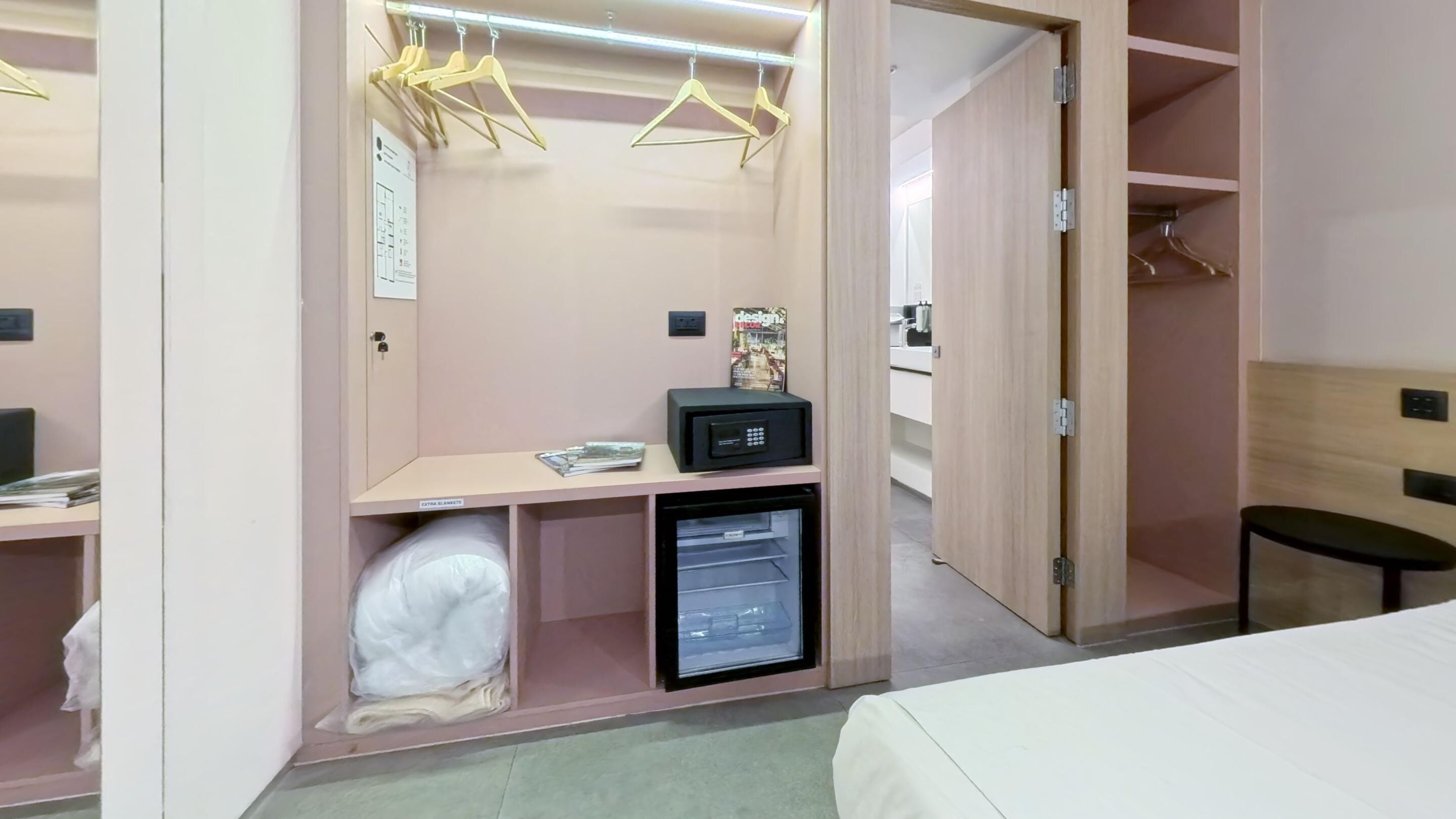Un dormitorio con cama, escritorio con computadora, refrigerador pequeño y armario con perchas.