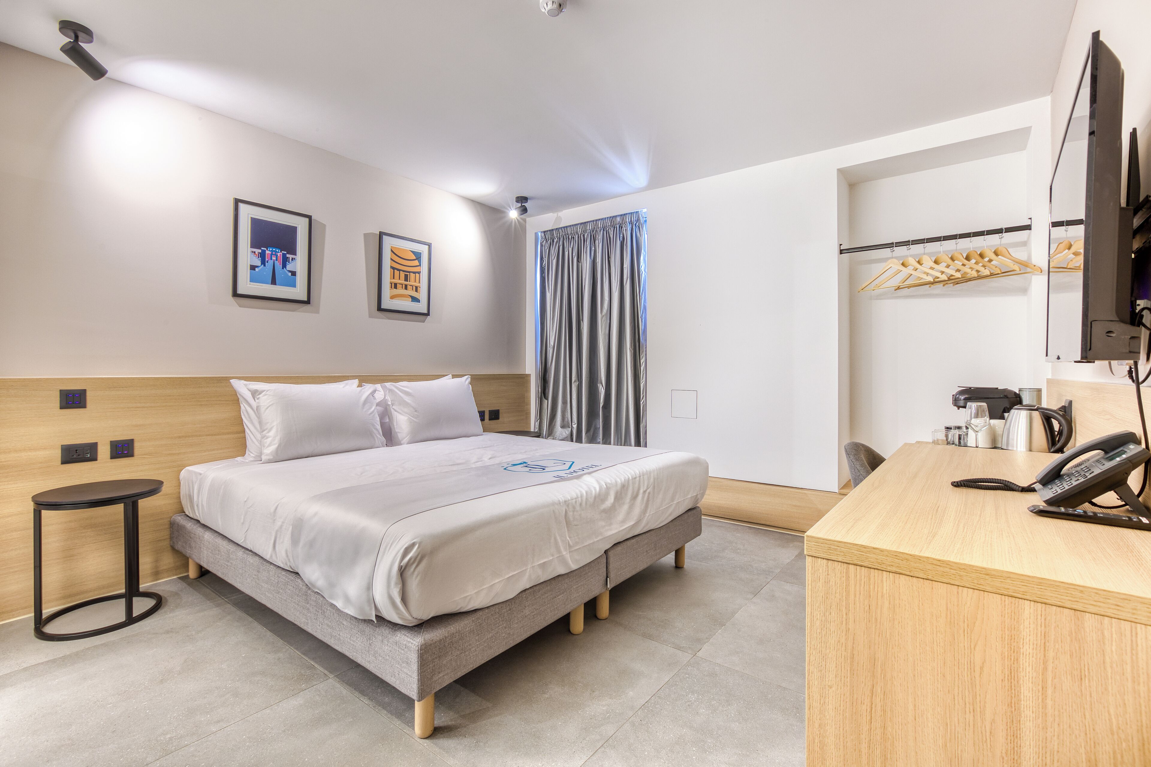 Una moderna camera d'albergo con un letto, un comodino e una scrivania con il telefono.