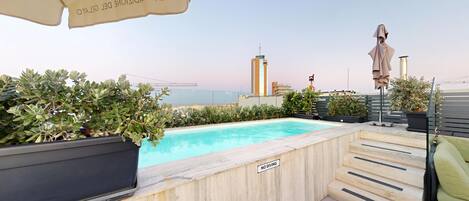 A rooftop pool with a 'NO DIVING' sign, potted plants, a staircase, and a view of the city skyline.
