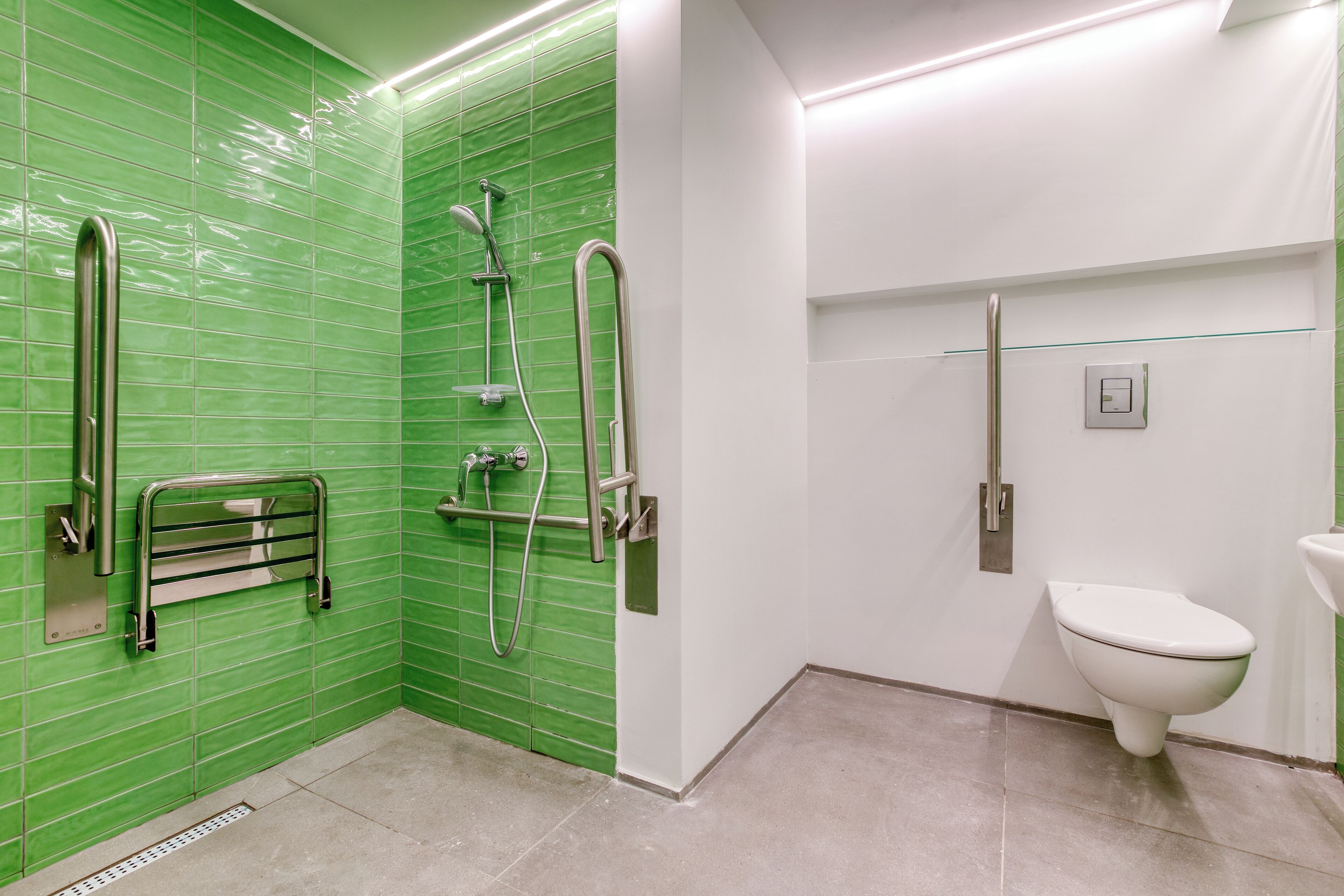 A bathroom with green tiled walls, a white toilet, and a shower with a handrail.