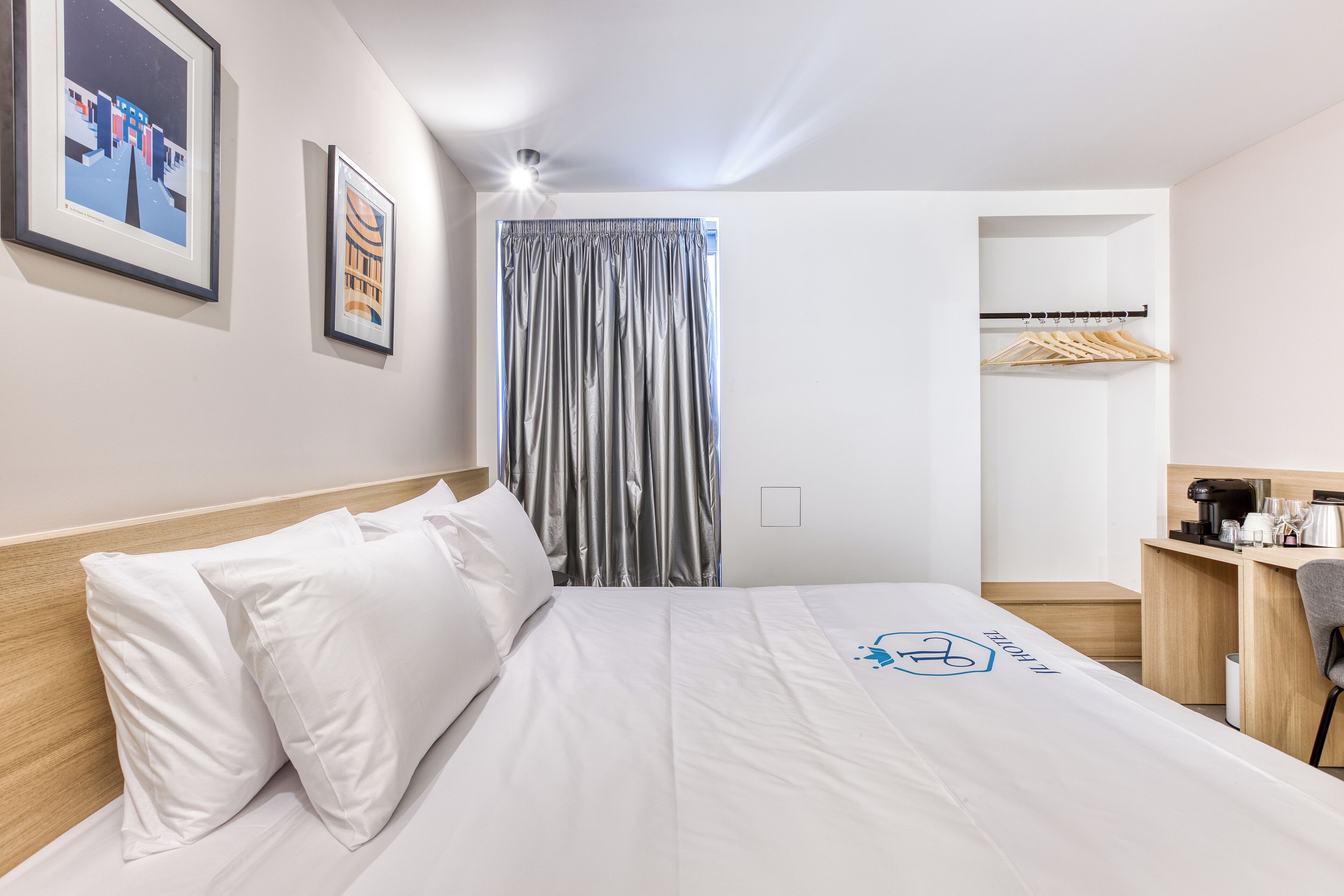 A hotel room with a bed, a desk, a chair, a wardrobe, and a window with curtains.