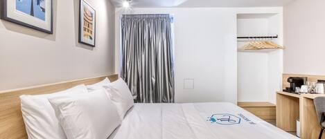 A hotel room with a bed, a desk, a chair, a wardrobe, and a window with curtains.