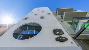Un moderno edificio de hotel con un tragaluz circular, un símbolo de corona y el texto "IL HOTEL" en la fachada.