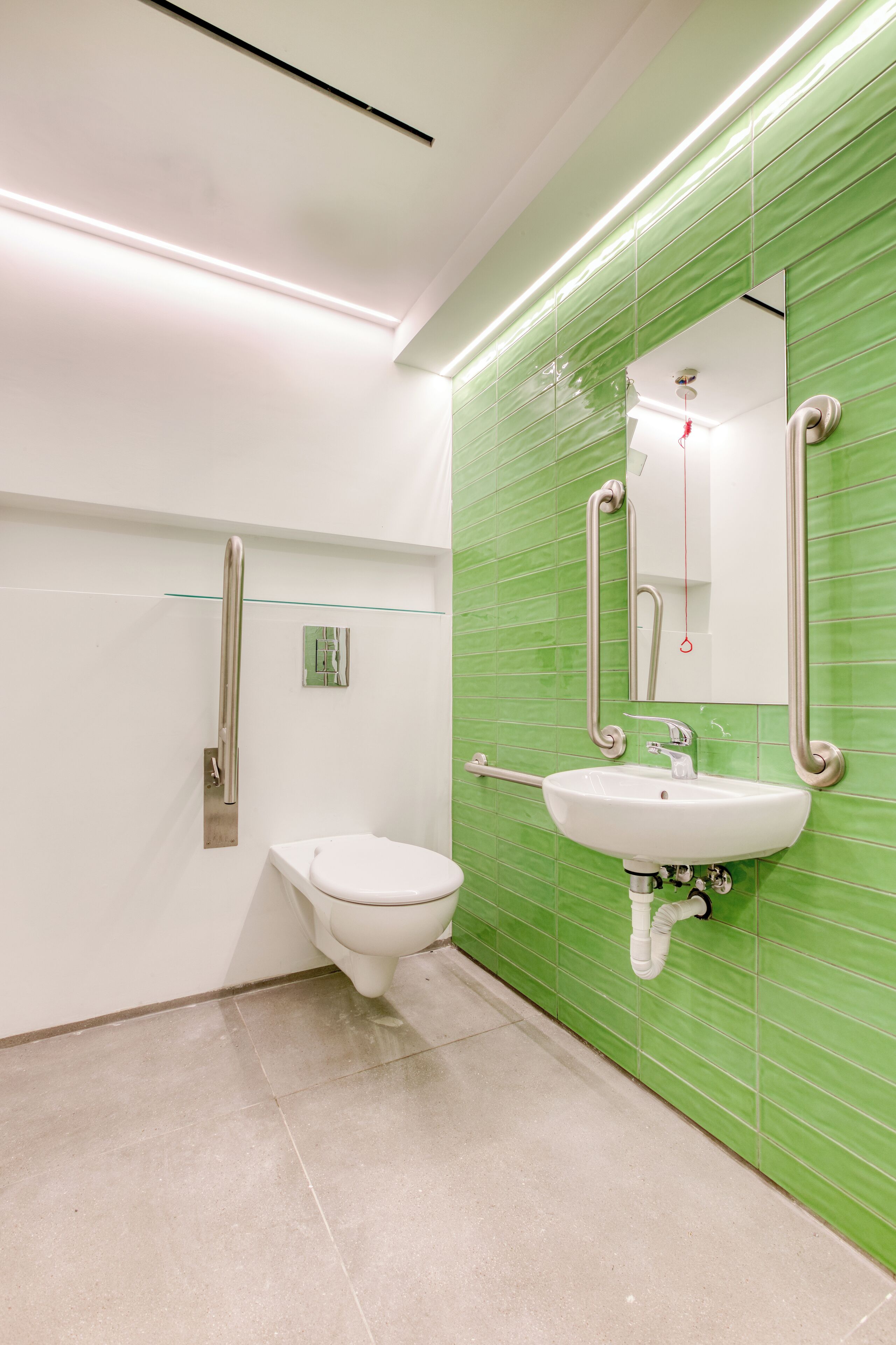A modern bathroom with a white toilet, a sink with a mirror, and green tiled walls.