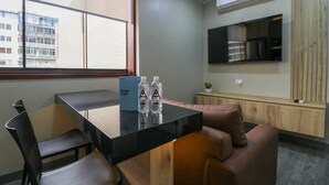 A modern room with a black table, two chairs, a sofa, a TV mounted on the wall, and a window with blinds.