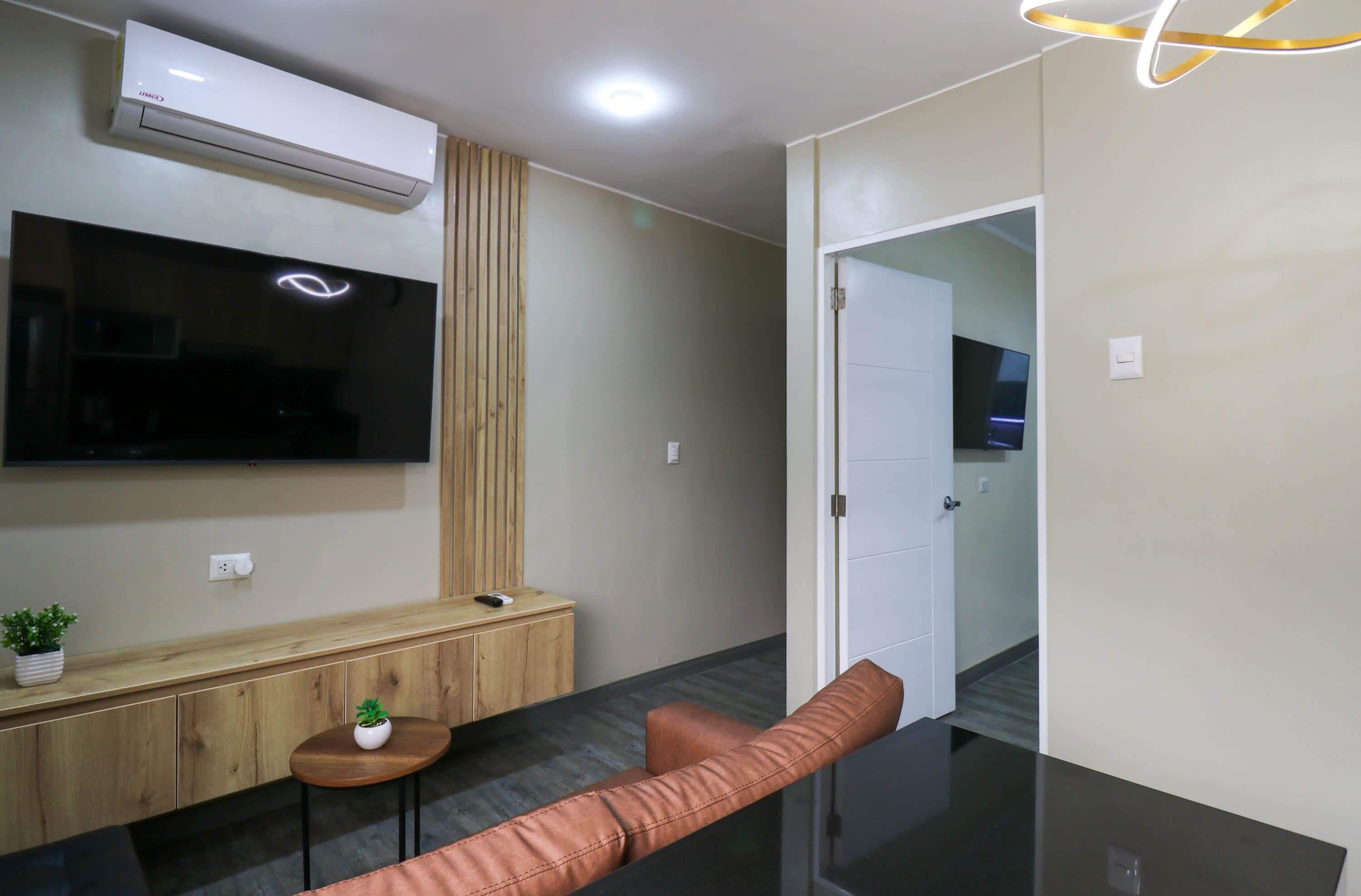 Een moderne woonkamer met een flatscreen televisie, een houten kast, een klein rond tafeltje met een plant en een leren bank.