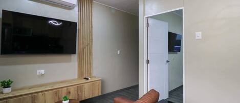 Een moderne woonkamer met een flatscreen televisie, een houten kast, een klein rond tafeltje met een plant en een leren bank.