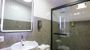 A modern bathroom with a large mirror, a sink, and a glass-enclosed shower.