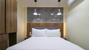 A neatly made bed with white linens, a wooden headboard, and two pendant lights above.