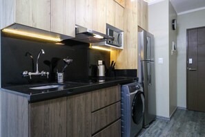A modern kitchen with wooden cabinets, a built-in microwave, a stainless steel refrigerator, a sink with a faucet, and a washing machine. - w* | Tranquil 1BR w/AC in San Isidro (San Isidro)