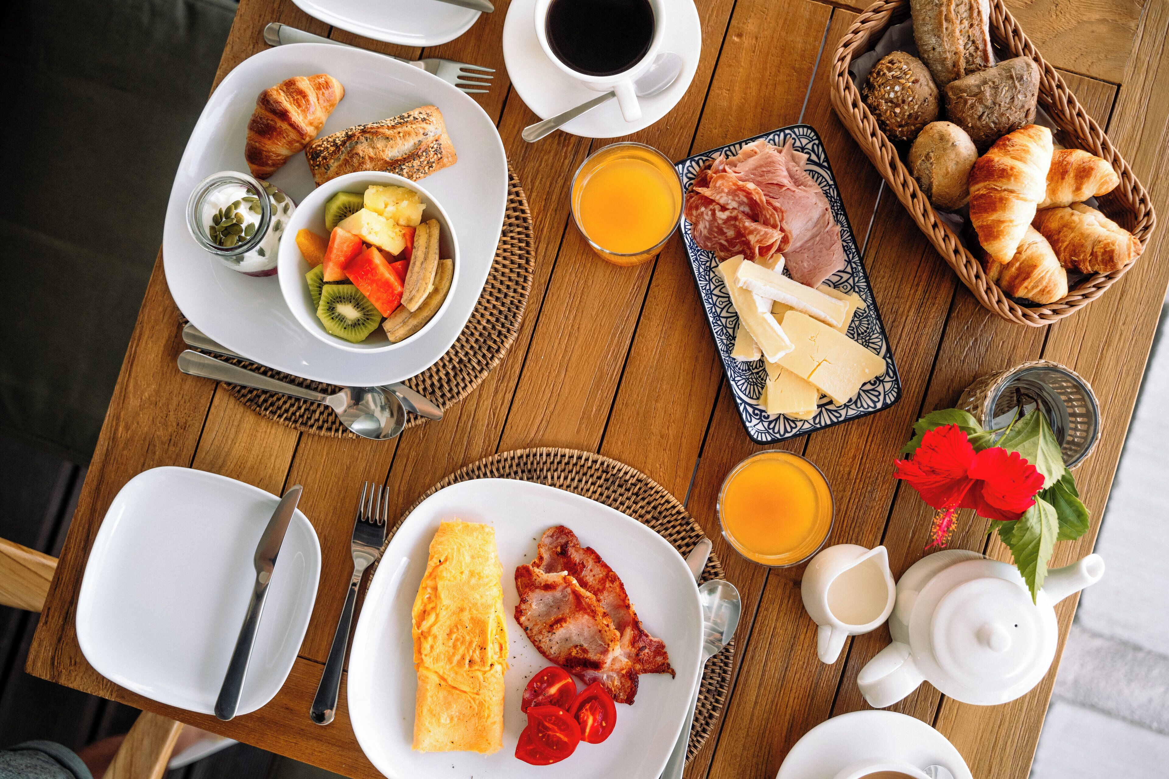 A breakfast table with croissants, cheese, ham, and fruit.