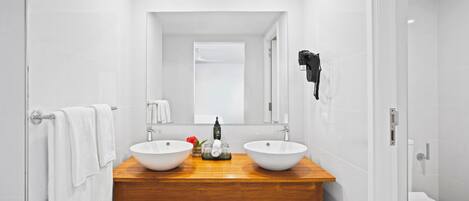 Un baño moderno con dos lavamanos blancos, un mueble de tocador de madera, un espejo y una zona de ducha.