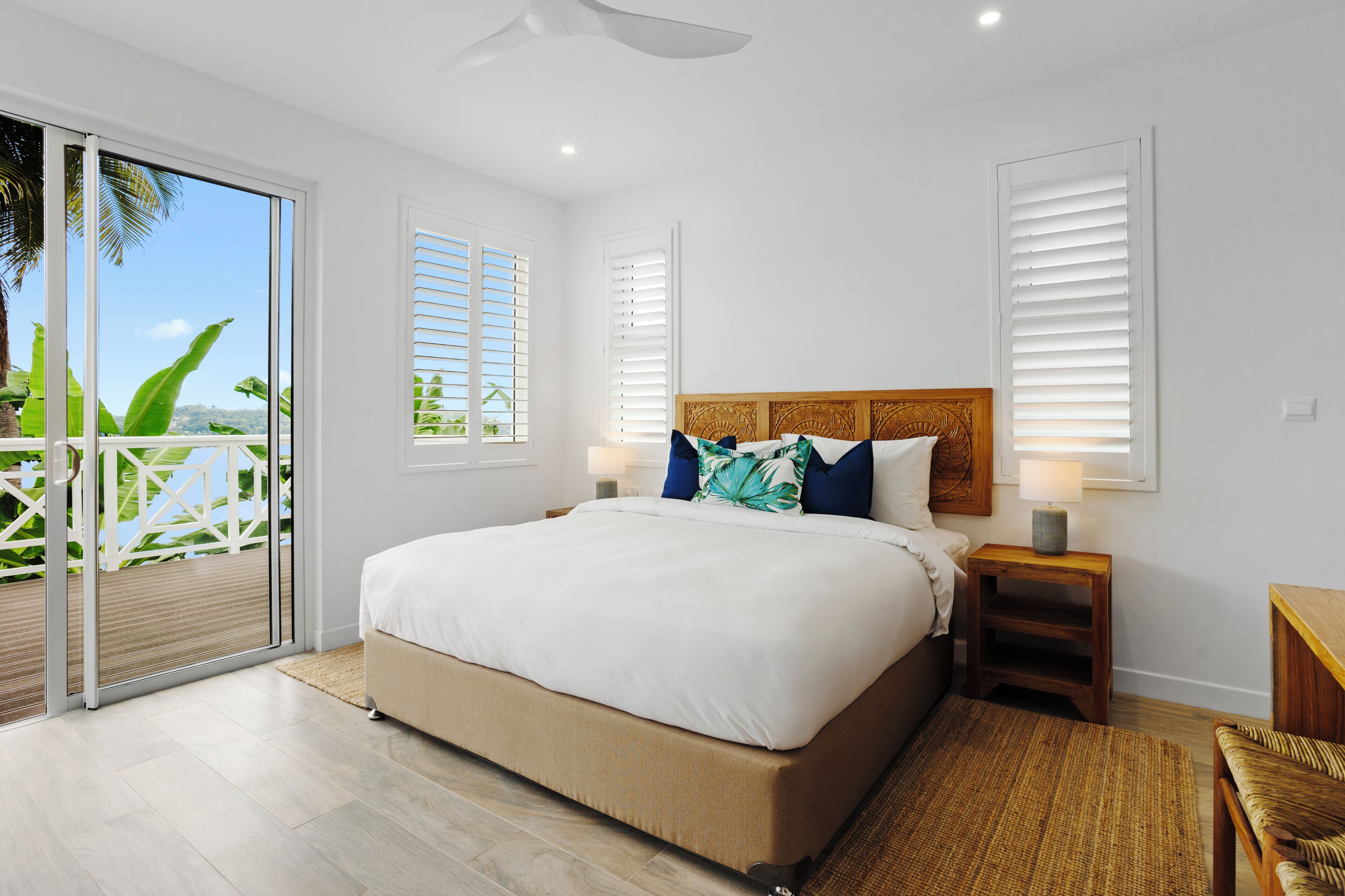 A bedroom with a large bed, a nightstand with a lamp, and a view of the outdoors through a sliding door.