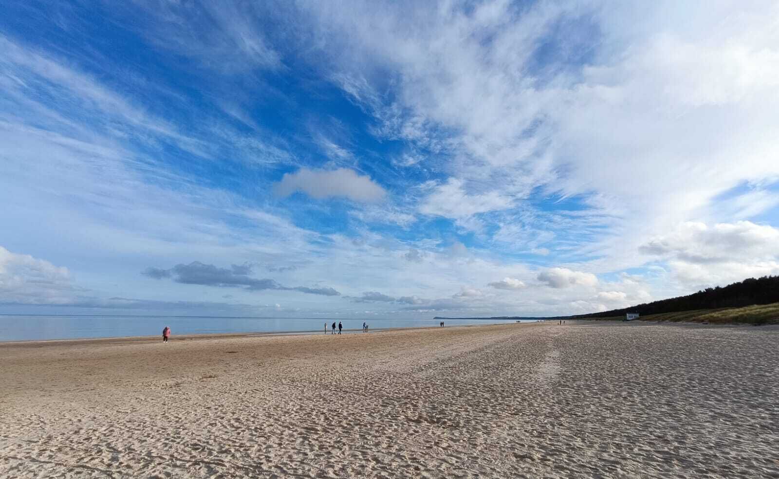 Une vaste plage de sable fin, un ciel dégagé et quelques personnes aperçues au loin.