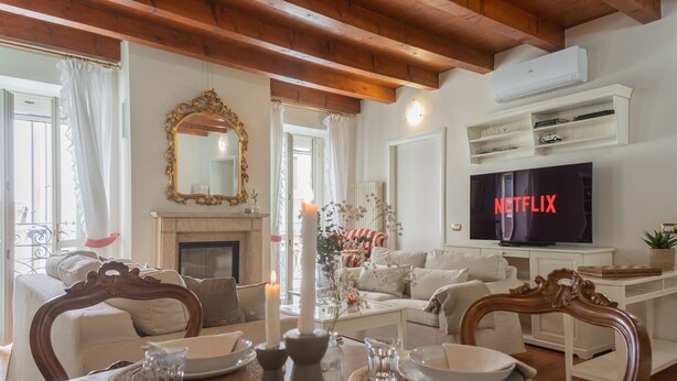 A living room with a fireplace, a television displaying 'NETFLIX', and a dining area with a table set for two. - Residenza Dolce Lago (Como)