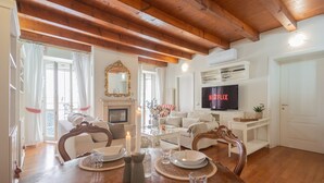 A living room with a wooden ceiling, a fireplace, a TV displaying Netflix, and a dining area set for four. - Residenza Dolce Lago (Como)