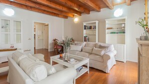 A spacious living room with wooden beams, a white sofa, a coffee table, and built-in bookshelves. - Residenza Dolce Lago (Como)