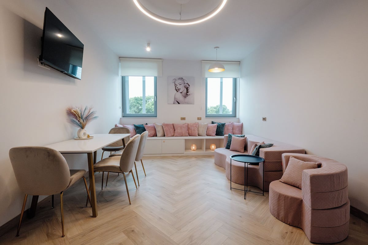 Una sala de estar moderna con comedor, un conjunto de sofás y un televisor montado en la pared.