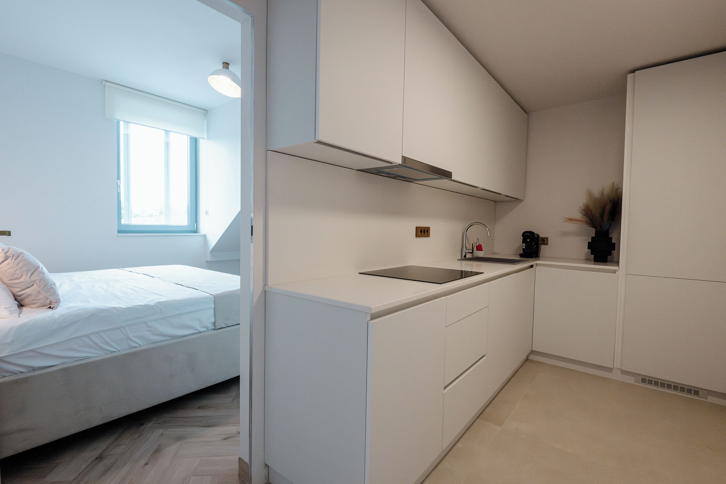 A compact, modern kitchen with white cabinetry, a built-in stove, and a window above the sink.