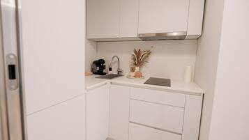 Una cocina compacta con armarios blancos, una campana extractora de acero inoxidable, una cafetera, un lavabo y un jarrón decorativo con plantas secas.