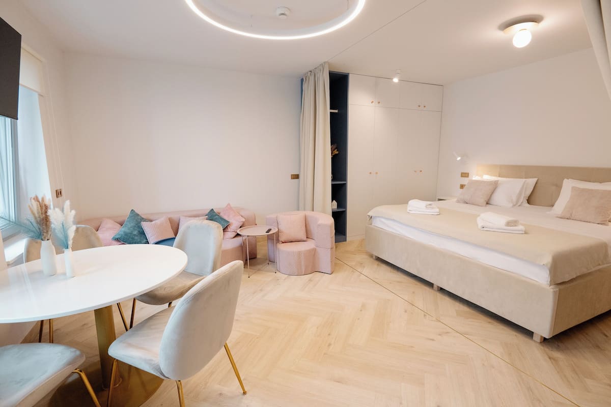Una habitación de hotel moderna con una cama grande, una mesa de comedor redonda y una zona de estar con sillas y sofá.