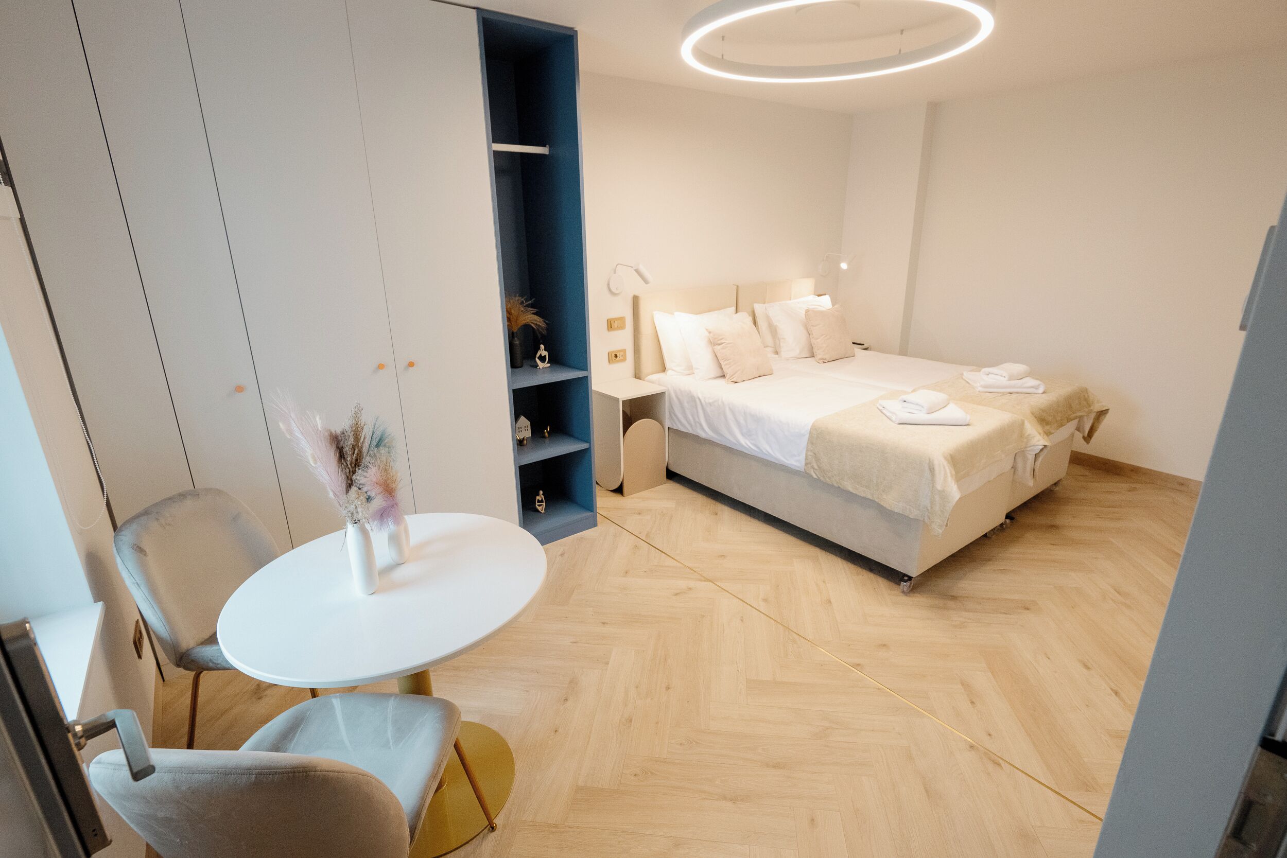 A modern hotel room with a bed, bedside tables, a round table, and a chair.