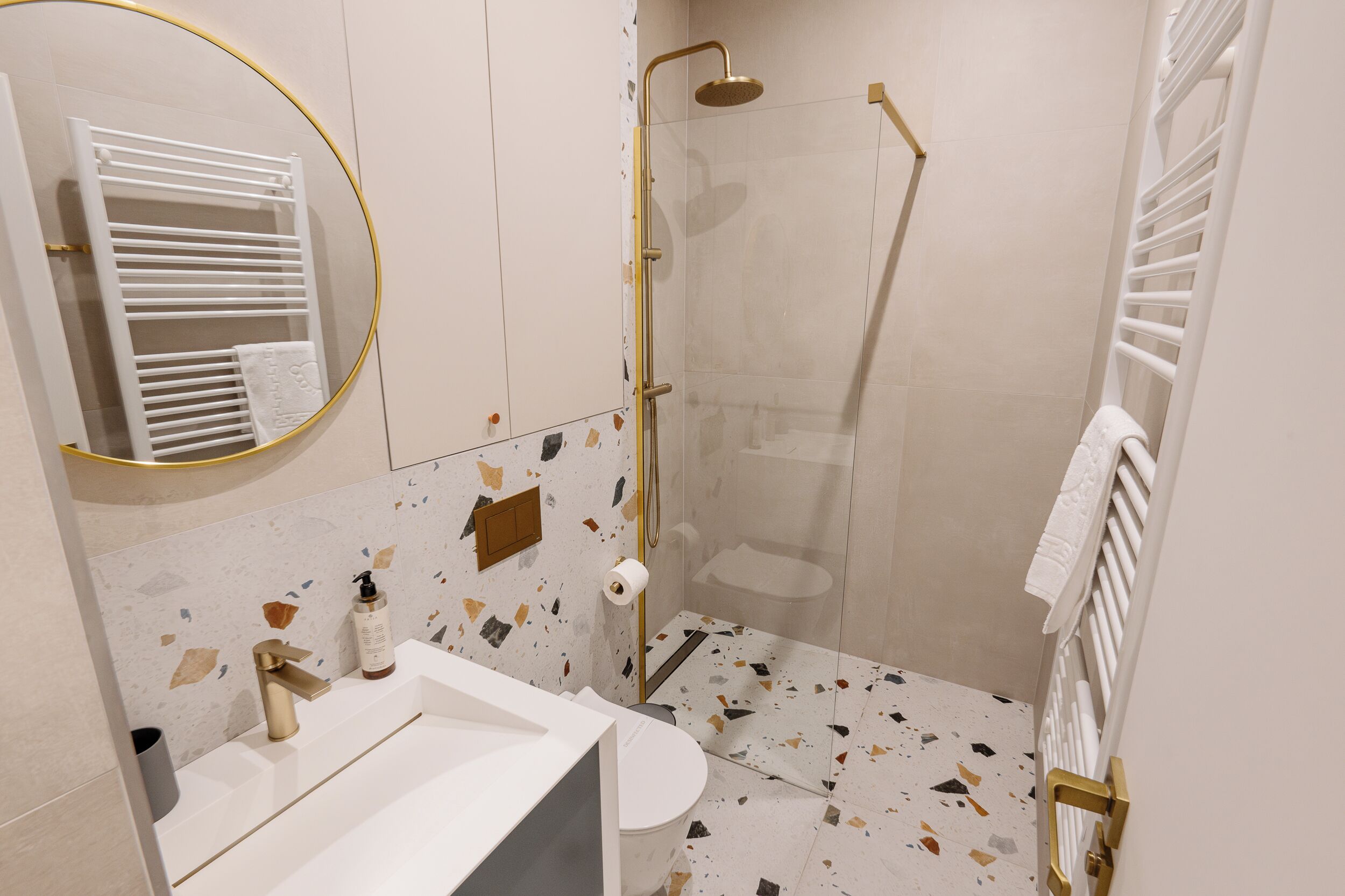 Un baño con lavamanos blanco, inodoro, ducha con puerta de cristal y un perchero para toallas.