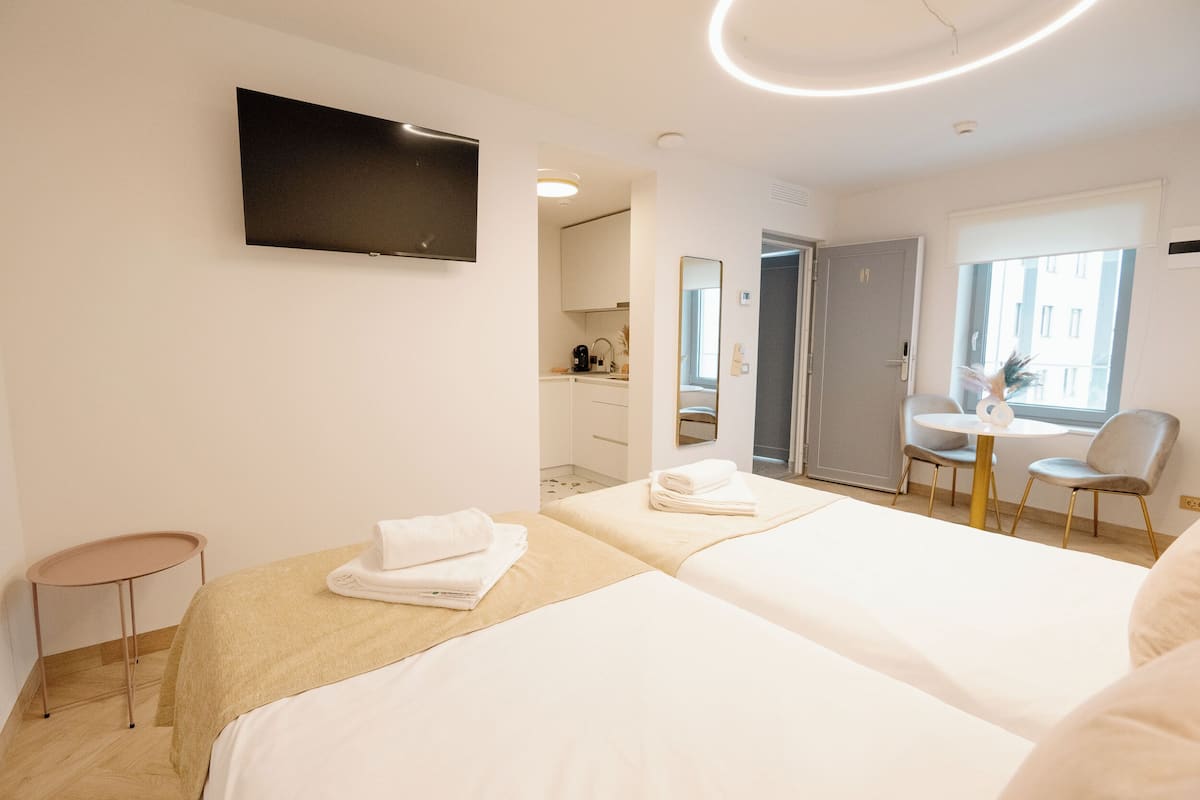 Habitación de hotel con dos camas, un televisor montado en la pared, una mesita y una silla.
