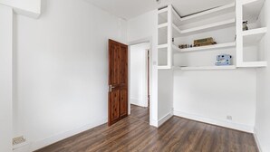 Ein Zimmer mit Holzboden, weißen Wänden und einer eingebauten Regaleinheit mit diversen Gegenständen.