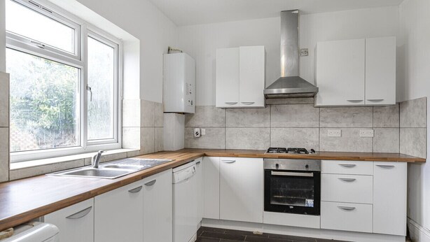 Eine moderne Küche mit weißen Schränken, einem eingebauten Backofen und einem Fenster, das natürliches Licht hereinlässt.