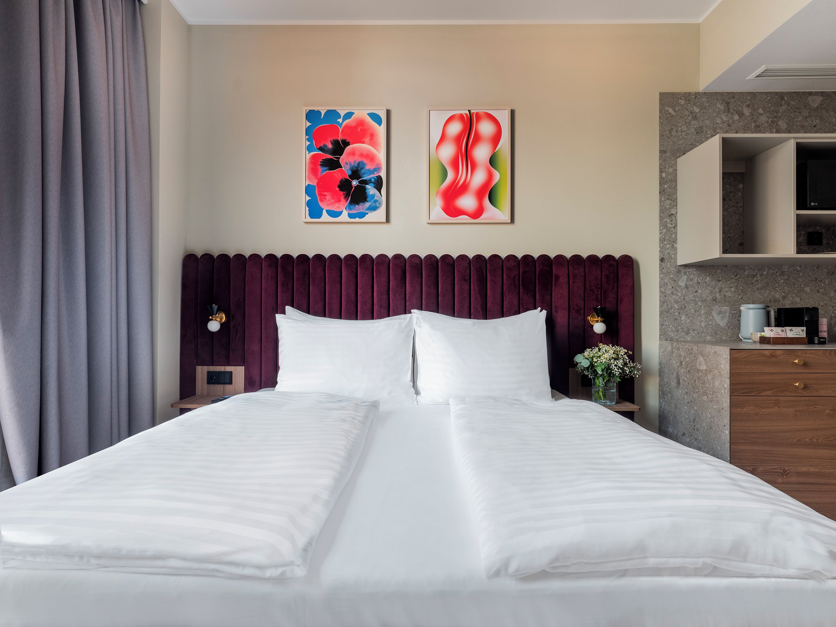 Une chambre d’hôtel moderne avec un grand lit, deux tables de chevet, un comptoir en marbre et des œuvres d’art accrochées au mur.