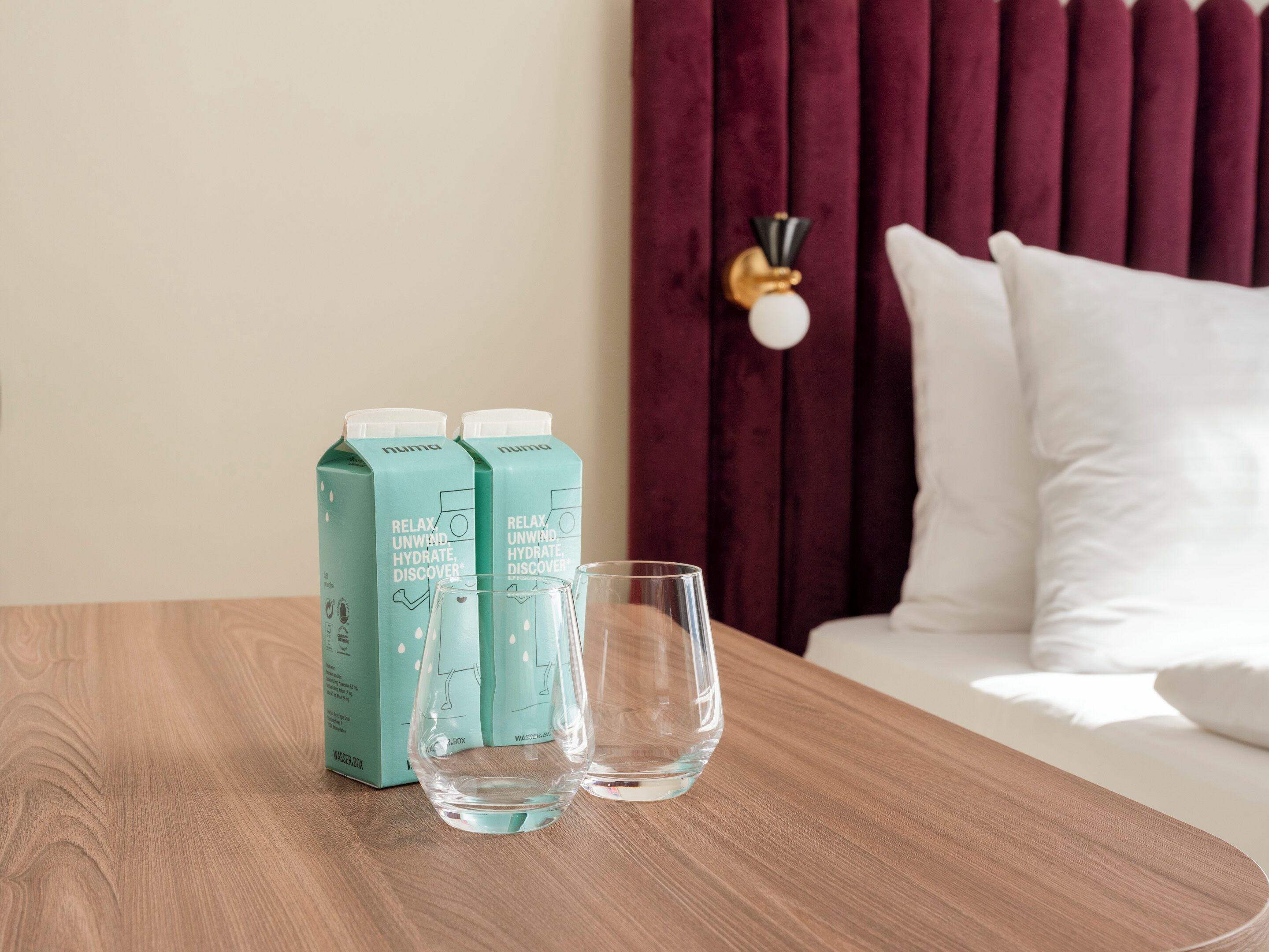 Una mesa de madera con dos botellas de agua color turquesa y dos vasos transparentes.