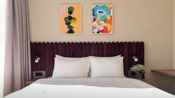 A hotel room with a bed, two wall-mounted lamps, a dark headboard, and two framed artworks.