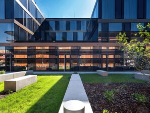 Un edificio moderno con amplios ventanales y un patio con césped y jardineras.