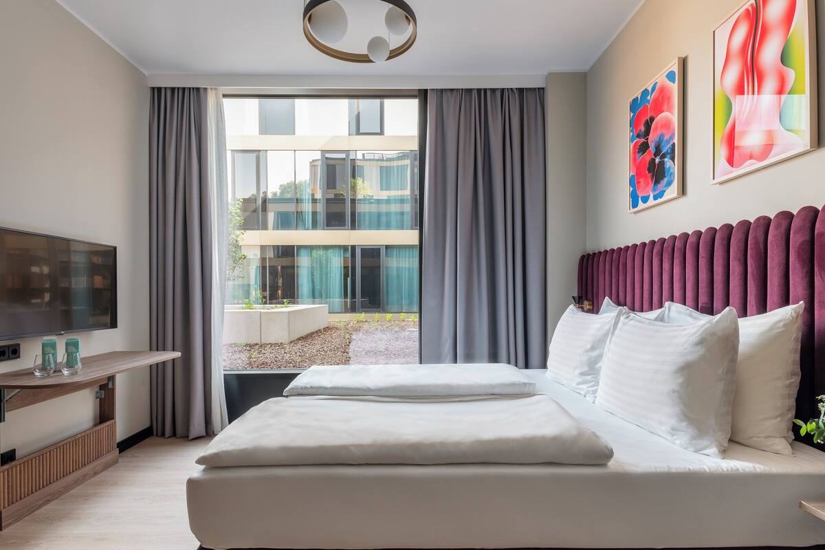 Une chambre d’hôtel moderne dotée d’un grand lit, d’un téléviseur à écran plat et offrant une vue sur l’extérieur.