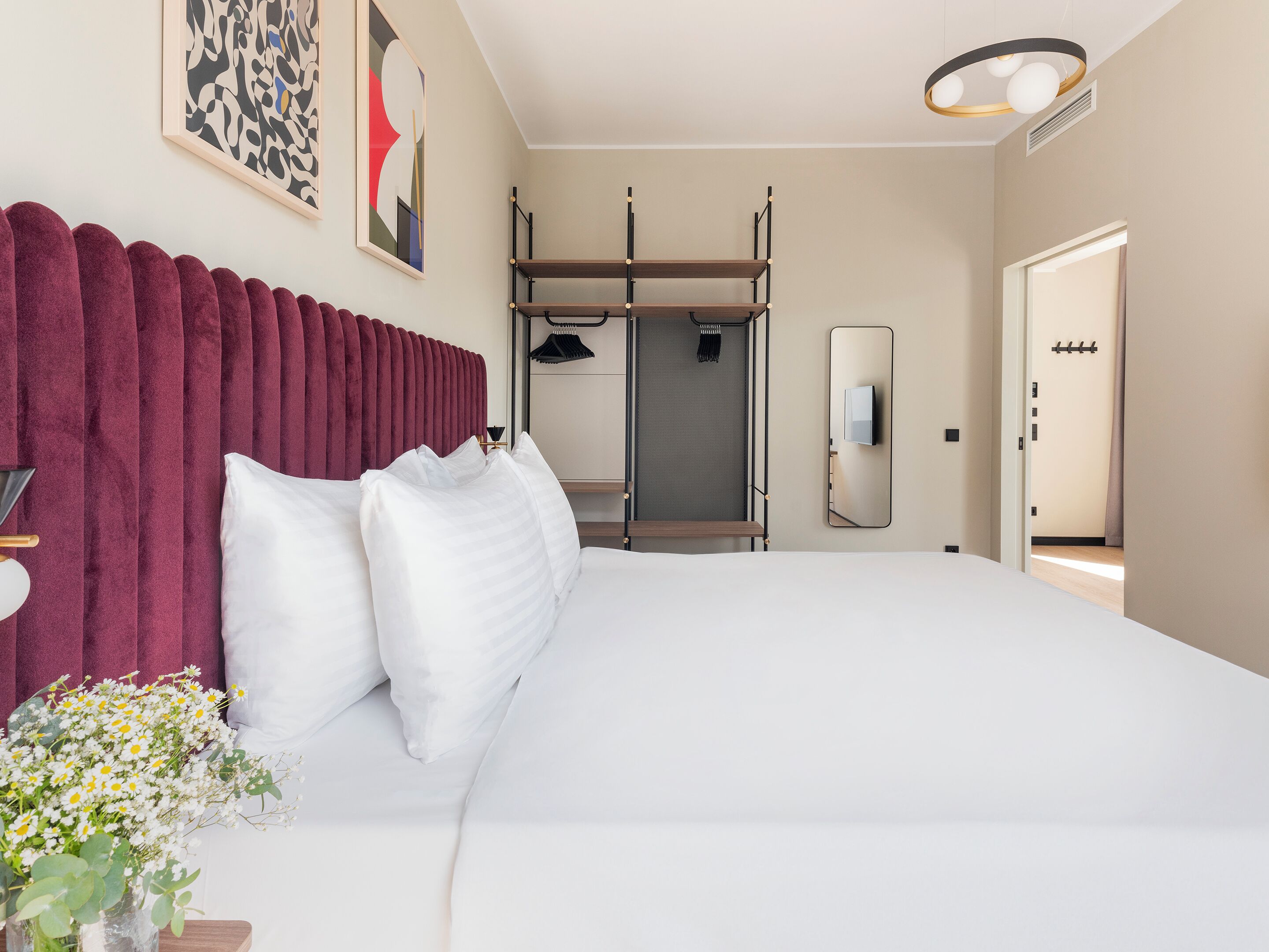 Ein modernes Hotelzimmer mit einem großen Bett, einem Schminktisch mit Spiegel und Blick auf den Flur.