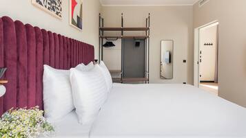 A modern hotel room with a large bed, a vanity with a mirror, and a view of the hallway.
