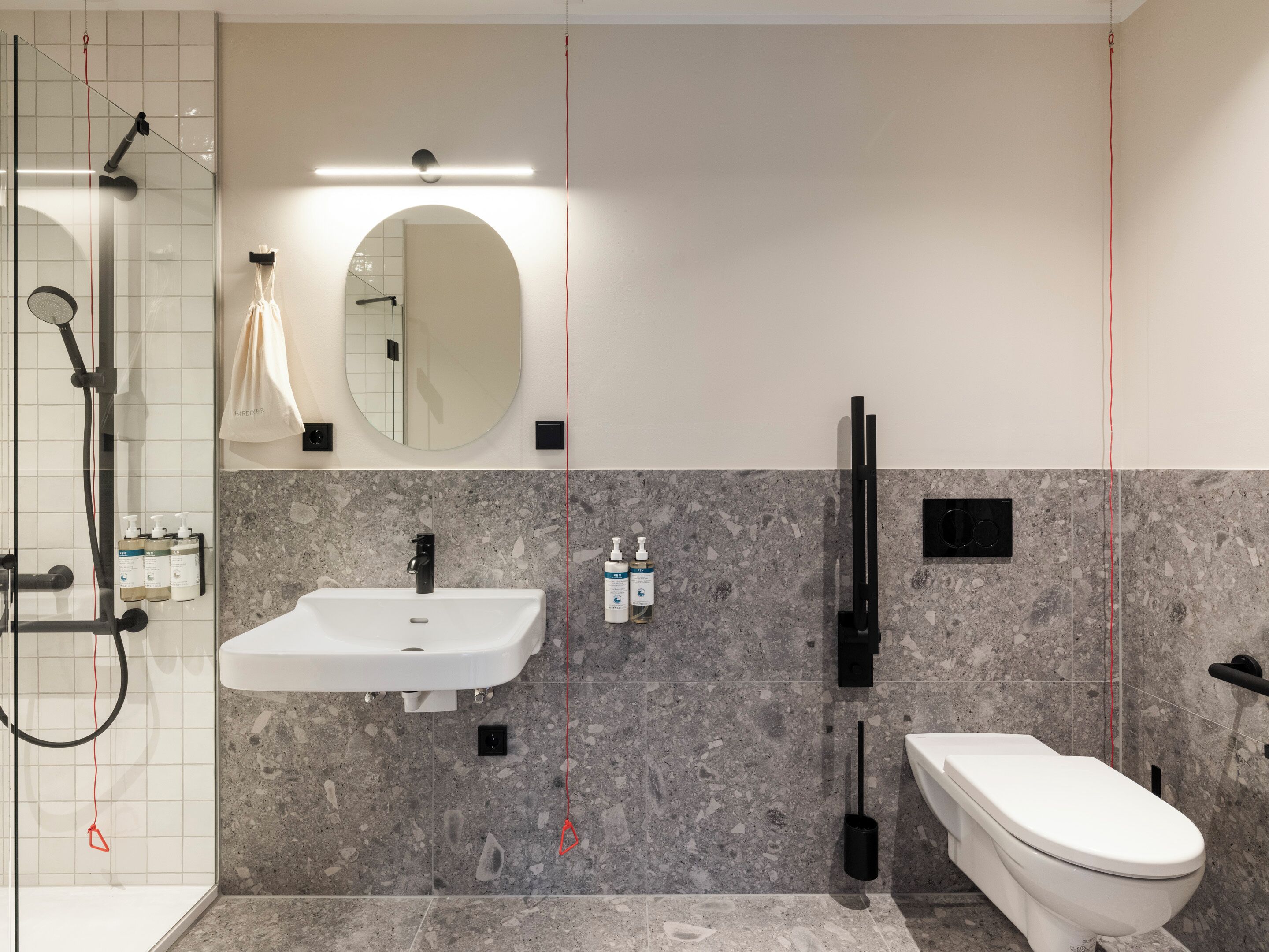A modern bathroom with a glass shower enclosure, a white sink, a toilet, and a marble-tiled wall.