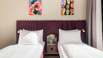 Ein Hotelzimmer mit zwei Betten, einem hölzernen Nachttisch mit Blumenvase und zwei Wandgemälden.