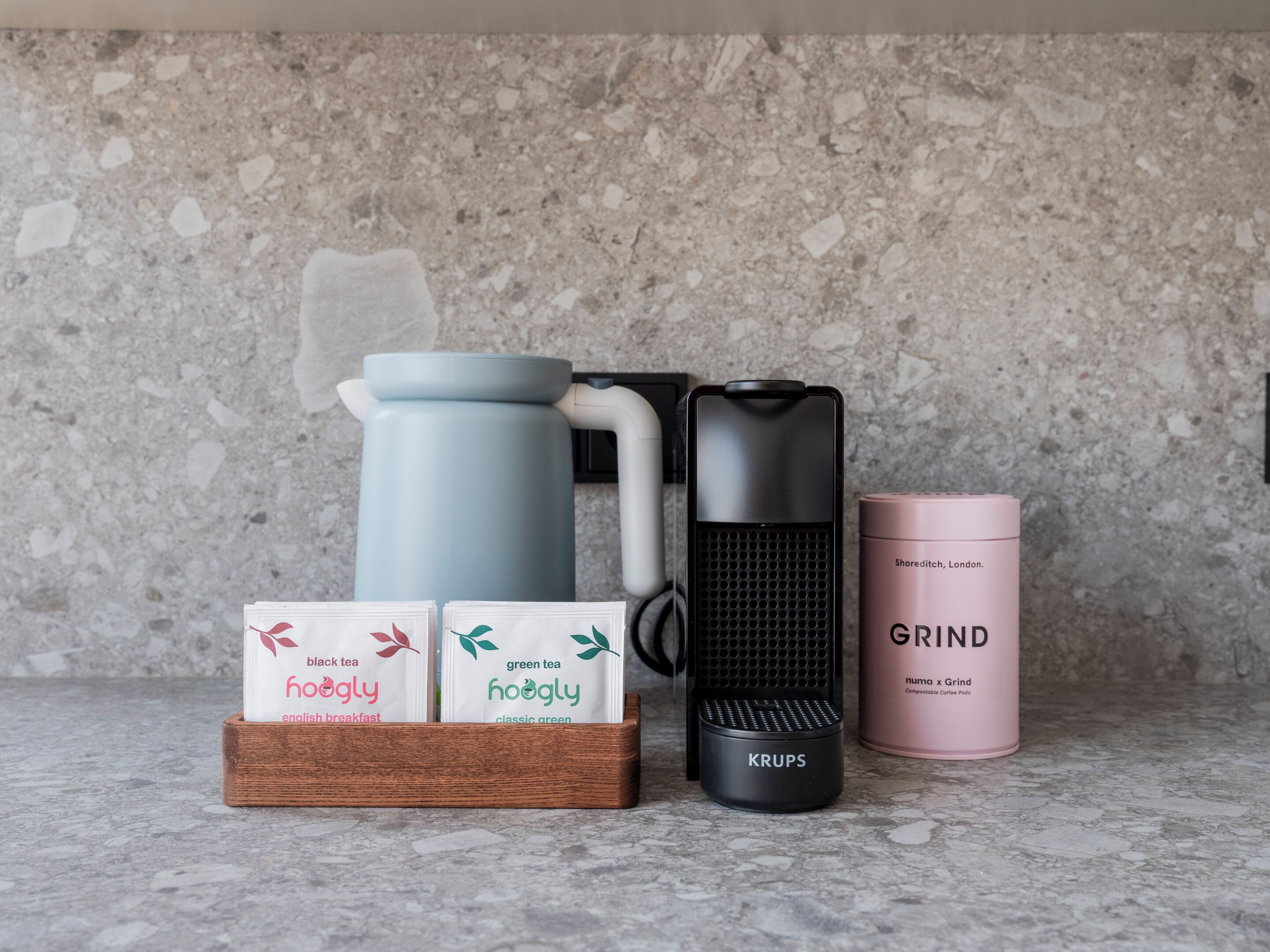 Una encimera de cocina con una cafetera, un molinillo y dos bolsitas de té etiquetadas 'hoogly'.