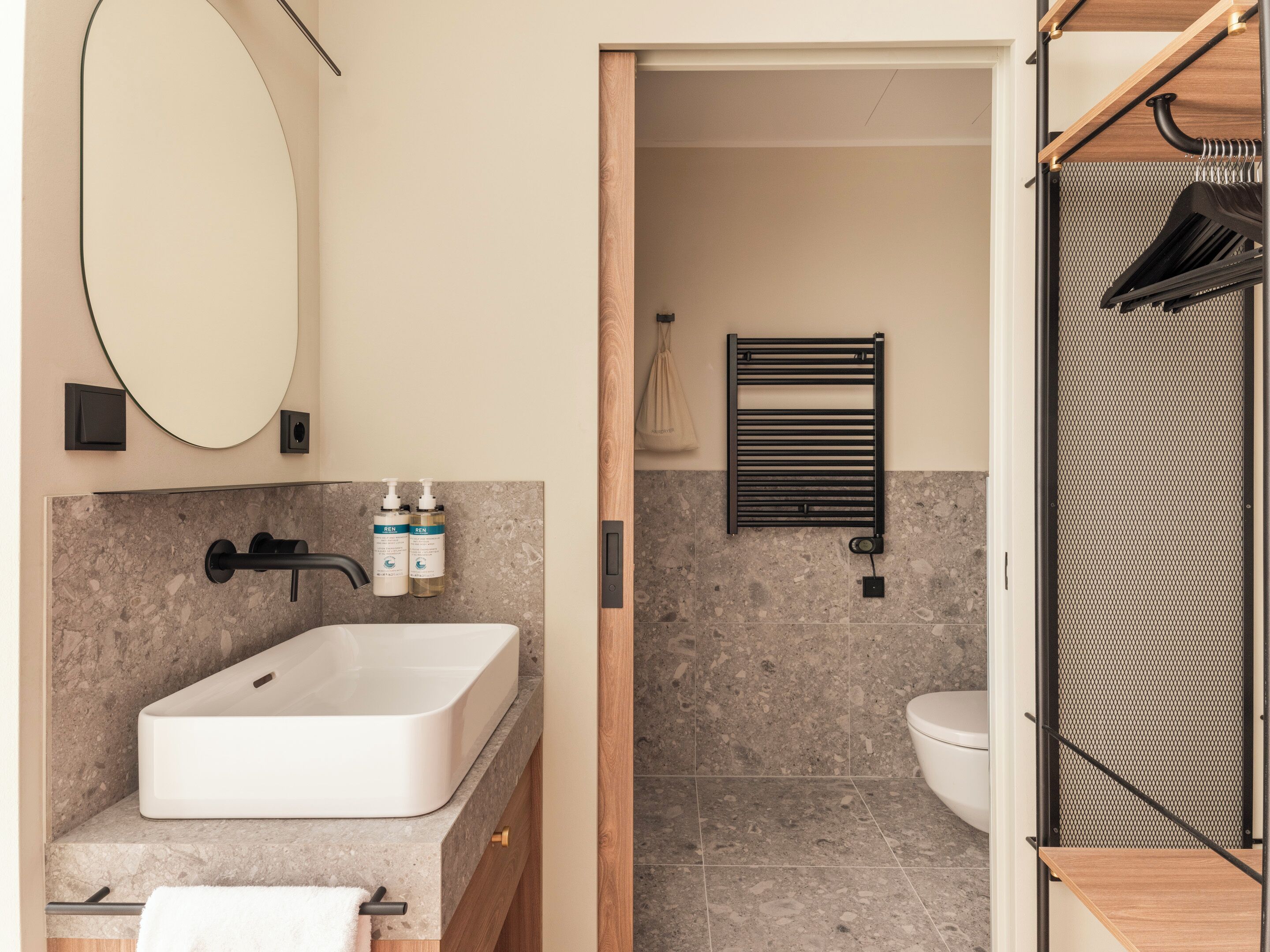 Une salle de bain moderne avec un grand miroir ovale, un lavabo blanc et deux flacons de savon liquide.