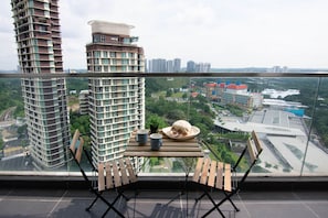 Uma varanda com mesa, duas cadeiras e vista para um horizonte urbano com edifícios altos e um rio.