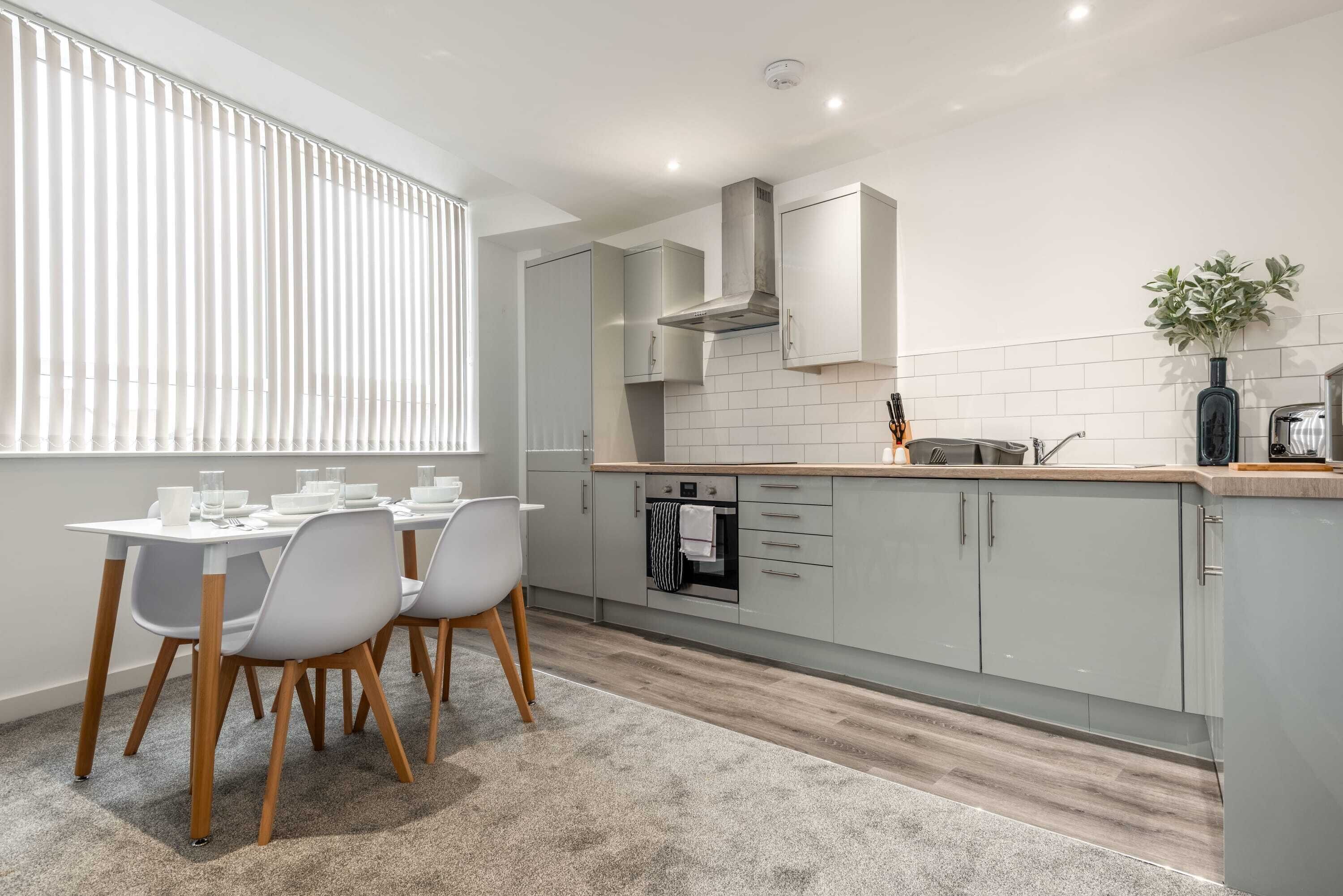 A modern kitchen with grey cabinets, a built-in oven, and a window with blinds.