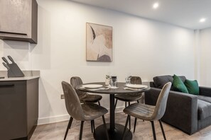 A modern dining area with a round table, four chairs, and a minimalist painting on the wall.