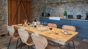Een rustieke eethoek met een houten tafel, rieten stoelen en een achtergrond van een stenen muur.