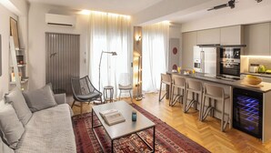 Een moderne woonkamer met een bank, salontafel en een keukenhoek, inclusief een koelkast, oven en barstoelen.