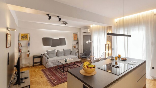 Een moderne woonkamer met een bank, salontafel en een eethoek met een fruitschaal en een klein barretje.