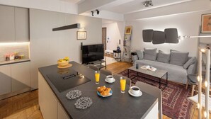 Een moderne keuken met een centraal eiland, een zithoek met een bank, en een woonkamer met een grijze bank en een televisie.